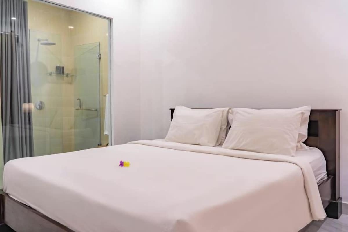 Habitación de hotel con cama, cabina de ducha de vidrio y tablero de cabecera de madera.
