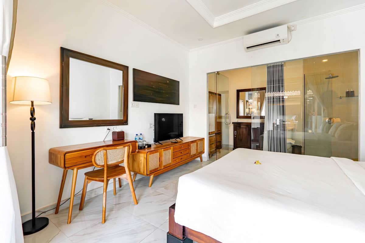 A hotel room with a bed, a desk with a chair, a television, and a large mirror.
