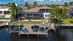 A waterfront property with a dock, kayaks, a swimming pool, and a covered patio area. - Ultimate Cape Coral home with Pool, Gulf Access & Games – Coral Horizon Villa (Cape Coral)