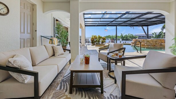 Eine sonnendurchflutete Terrasse mit einer Couch, Stühlen und einem Tisch, mit Blick auf einen Swimmingpool und den Himmel.