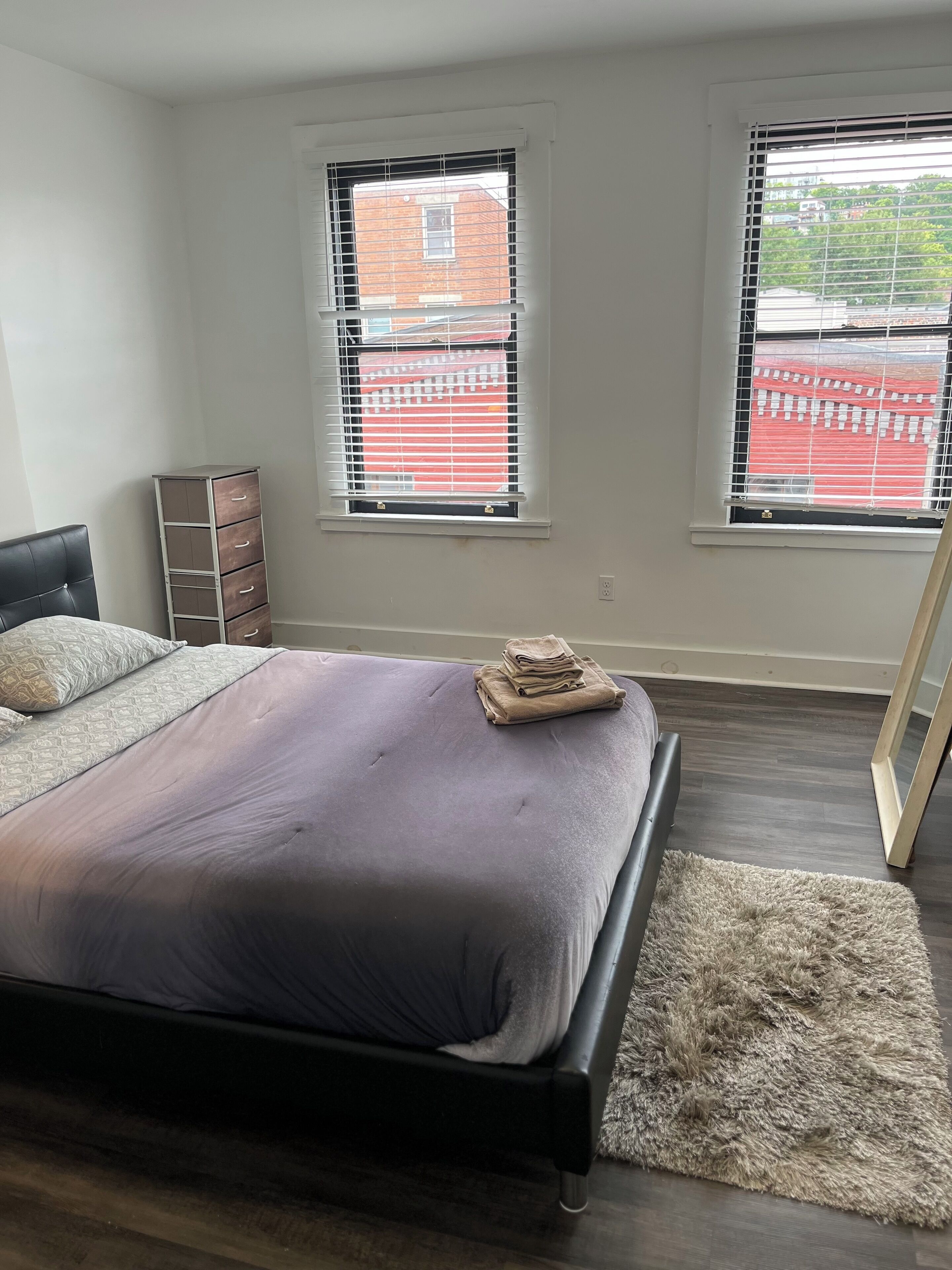 A bedroom with a bed, a dresser, and two windows with blinds.