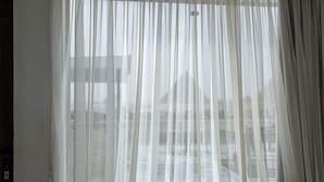 A window with sheer white curtains, a view of buildings outside, and a visible light switch on the wall.