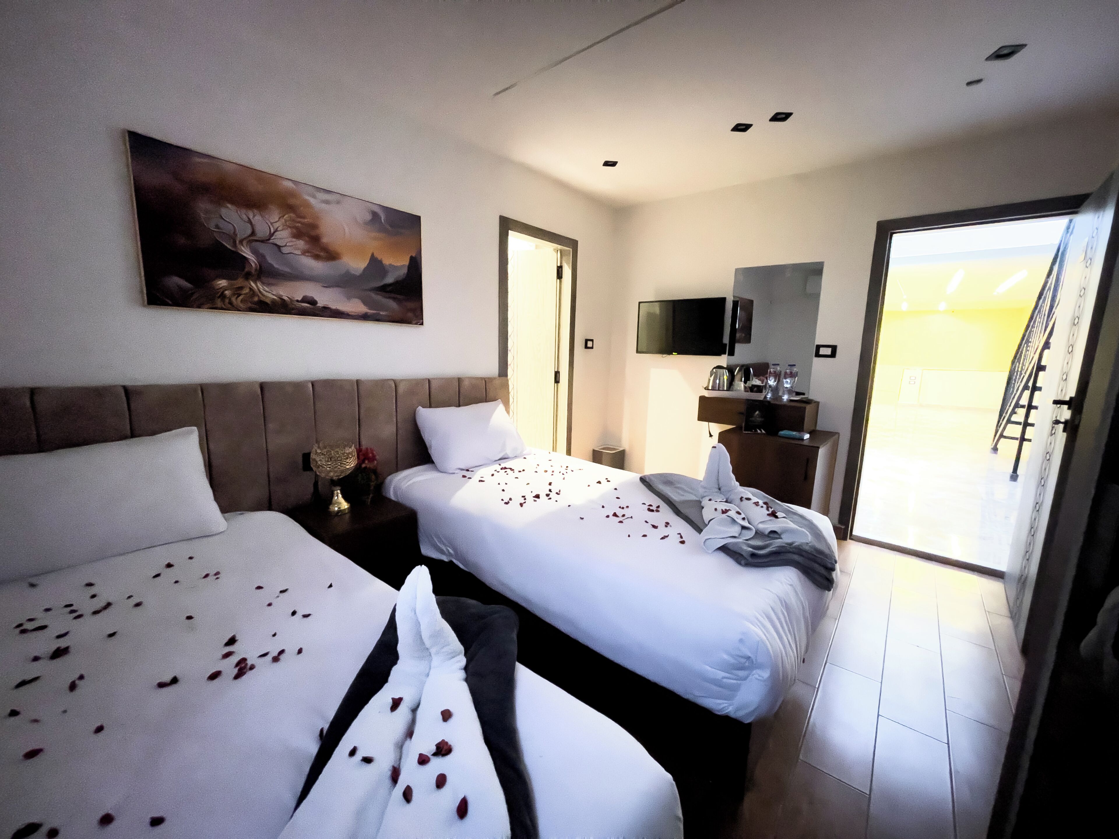 Quarto de hotel com duas camas, um quadro, uma televisão e uma varanda.