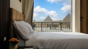 A hotel room with a bed, a vase with flowers, and a view of the pyramids.
