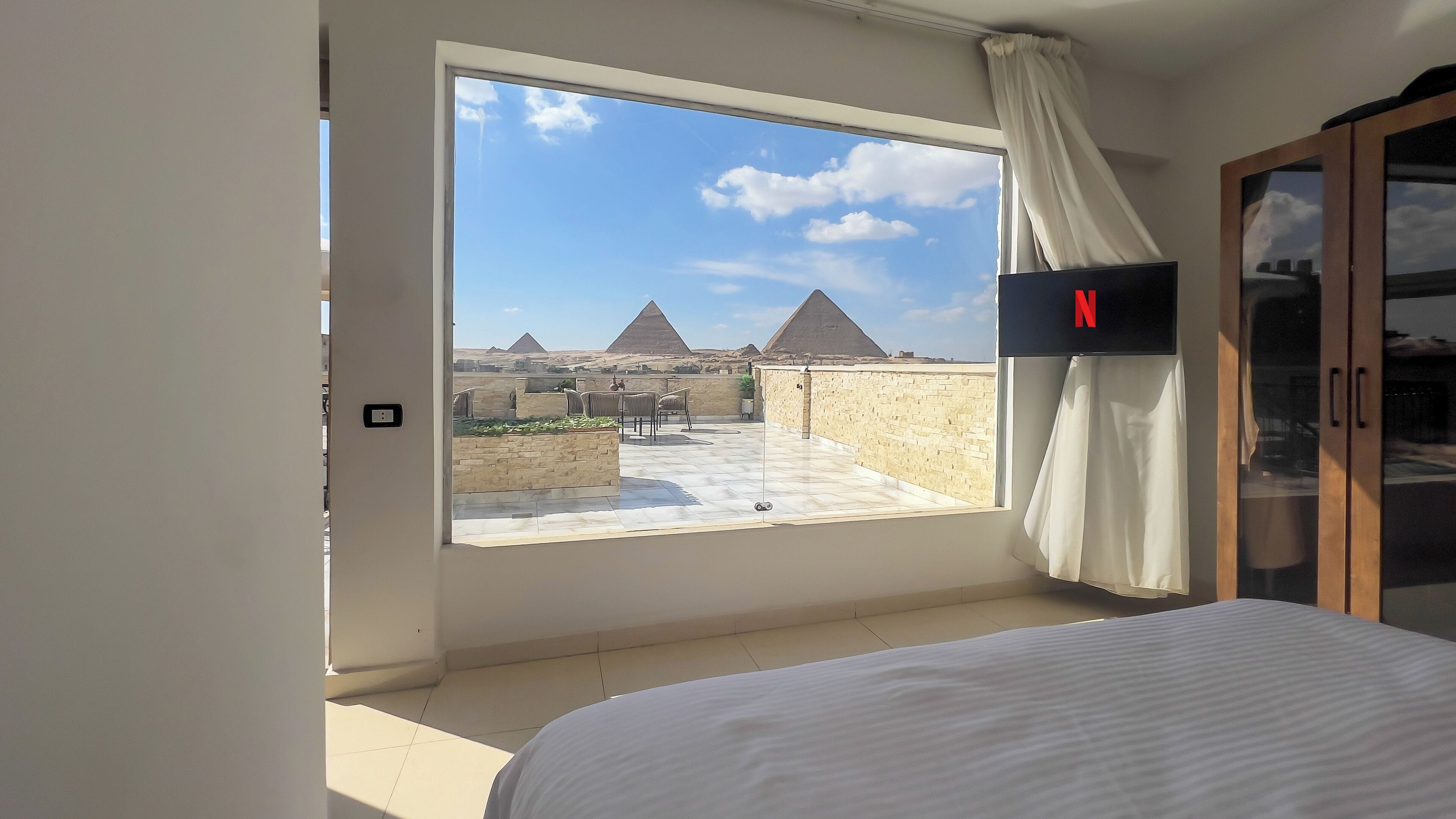 Quarto de hotel com uma grande janela que oferece vista para pirâmides.