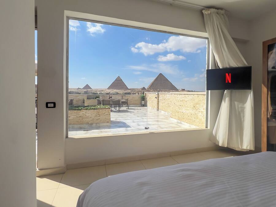 Habitación de hotel con un ventanal grande que ofrece vistas a las pirámides.
