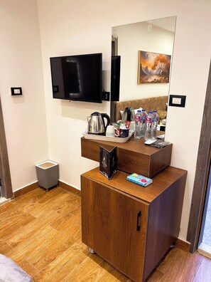 A hotel room with a wooden cabinet, a television mounted on the wall, a painting, and a small trash bin. - Point Pyramids View Inn (Giza)