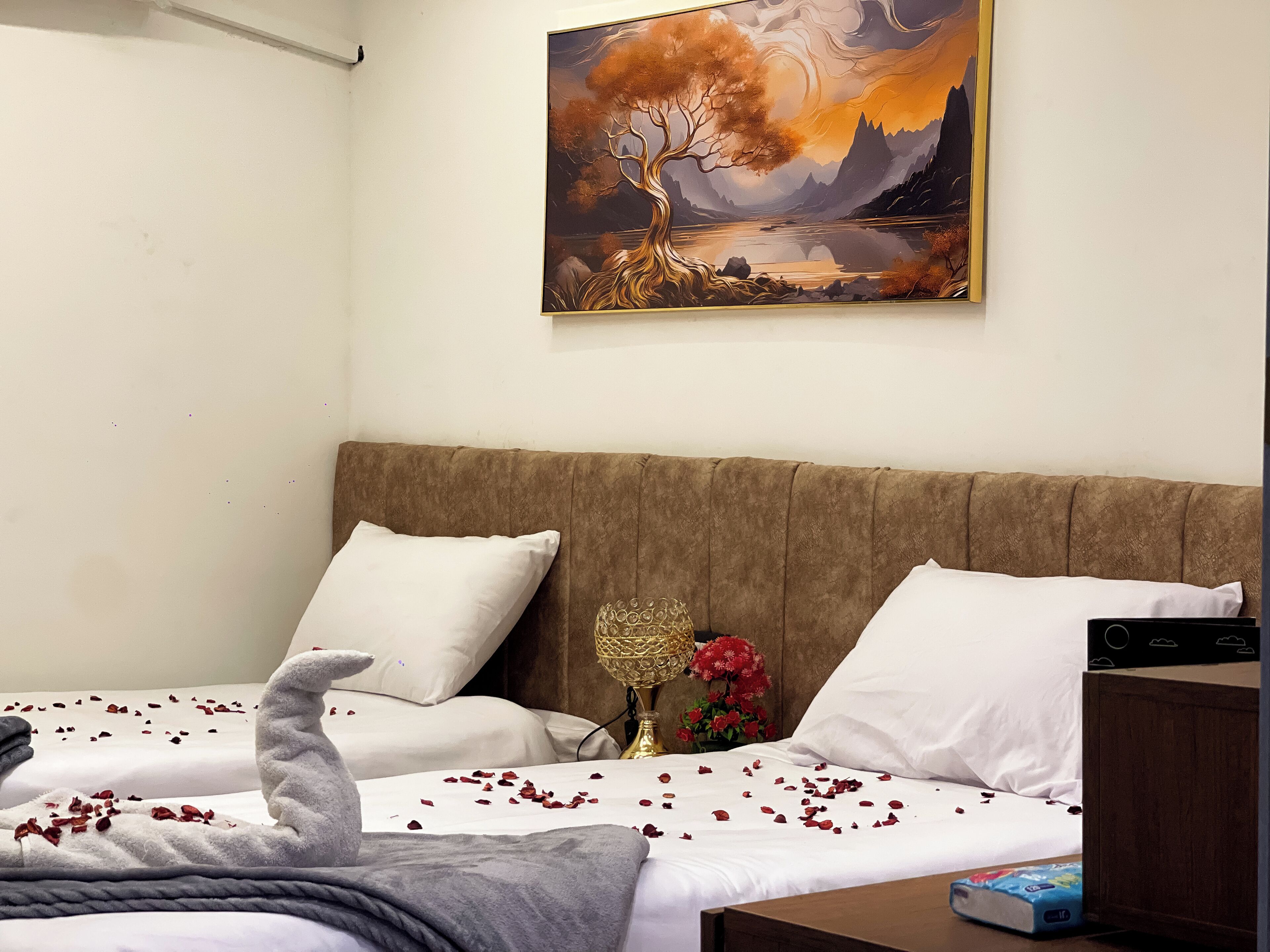 A bedroom with a bed, pillows, a bedside table, a lamp, and a painting on the wall.