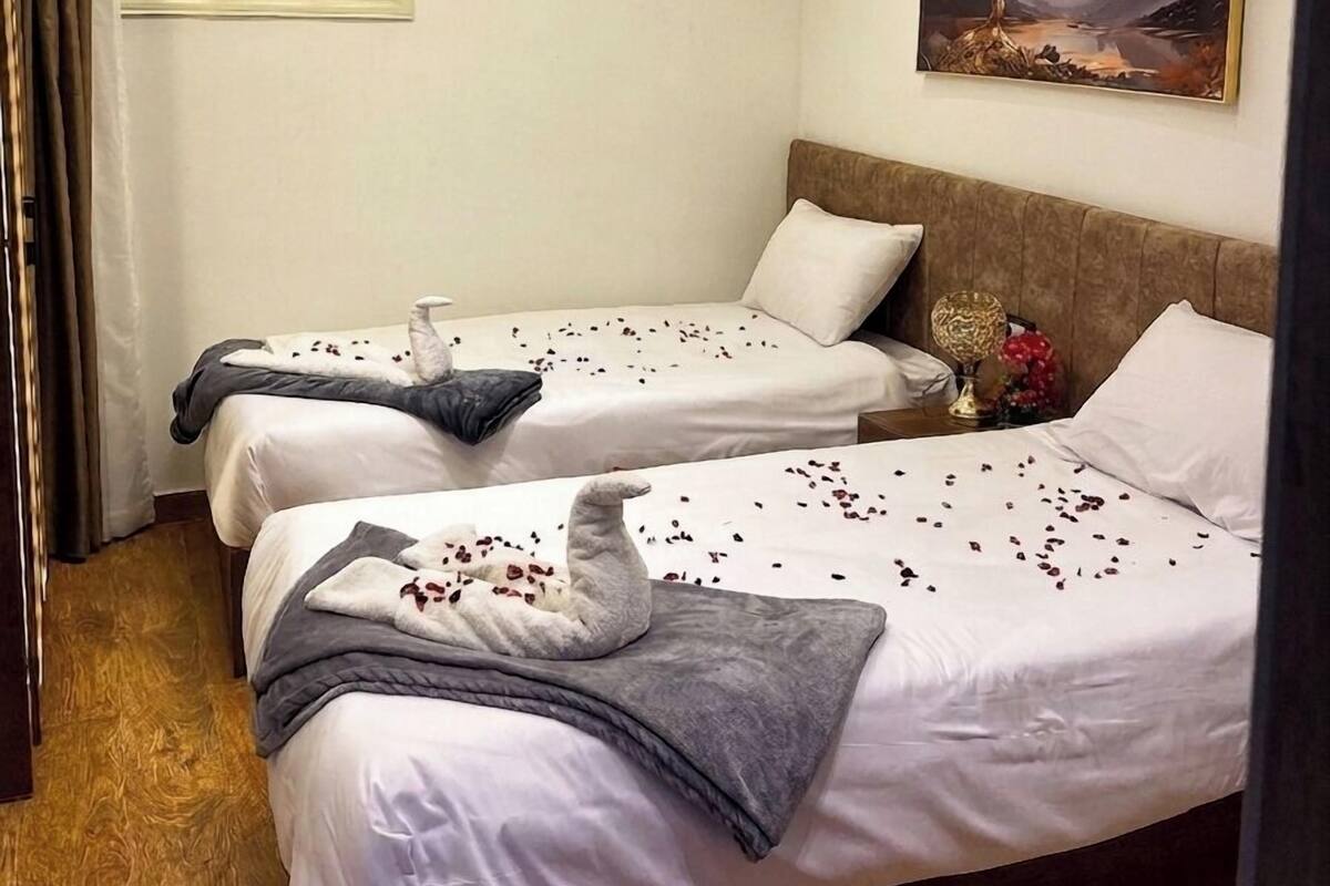 Ett hotellrum med två sängar, en luftkonditioneringsanläggning, en tavla på väggen och ett fönster med utsikt över en pyramid.