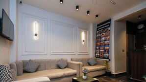 A modern lobby with a beige sofa set, patterned pillows, a small table with a vase, and a wall-mounted TV.