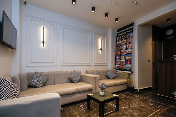 A modern lobby with a beige sofa set, patterned pillows, a small table with a vase, and a wall-mounted TV. - Point Pyramids View Inn (Giza)