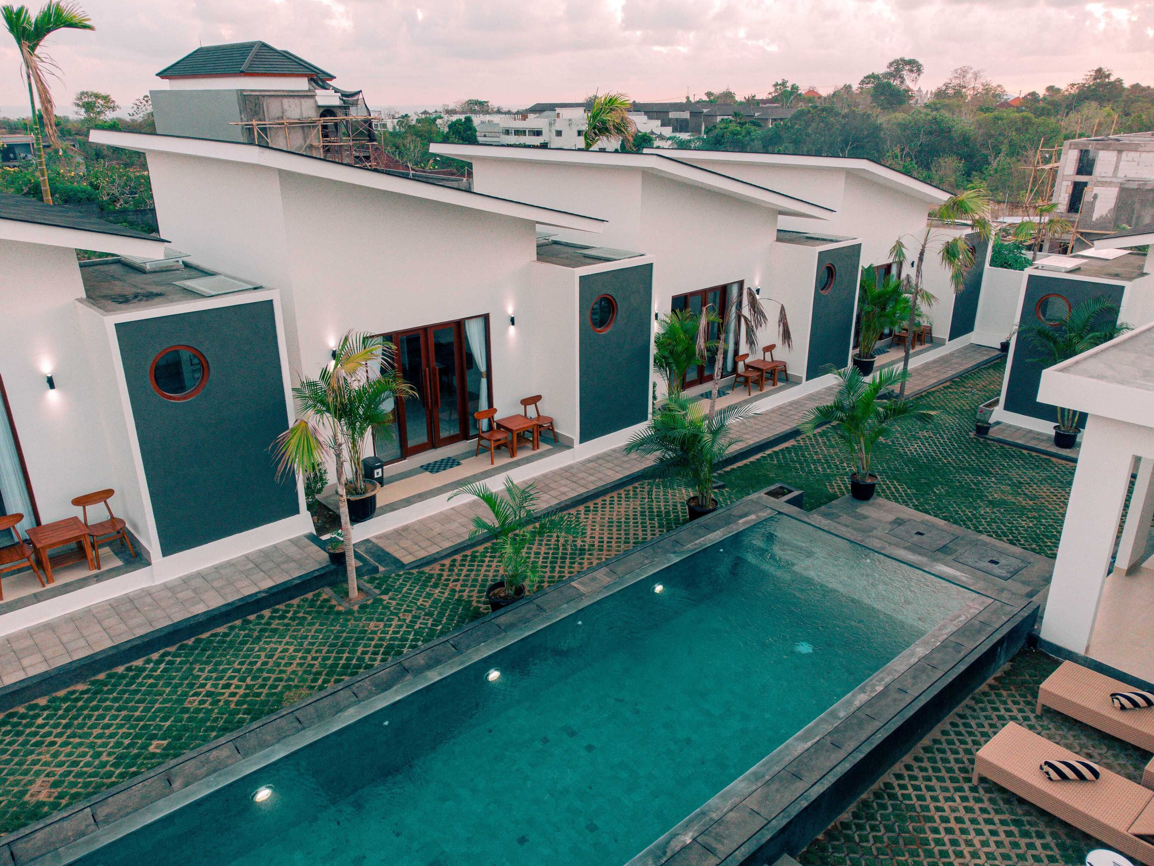 Un hotel moderno con piscina, zona de estar exterior y abundante vegetación.