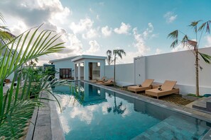 Une piscine avec des chaises longues, des palmiers et un bâtiment moderne.