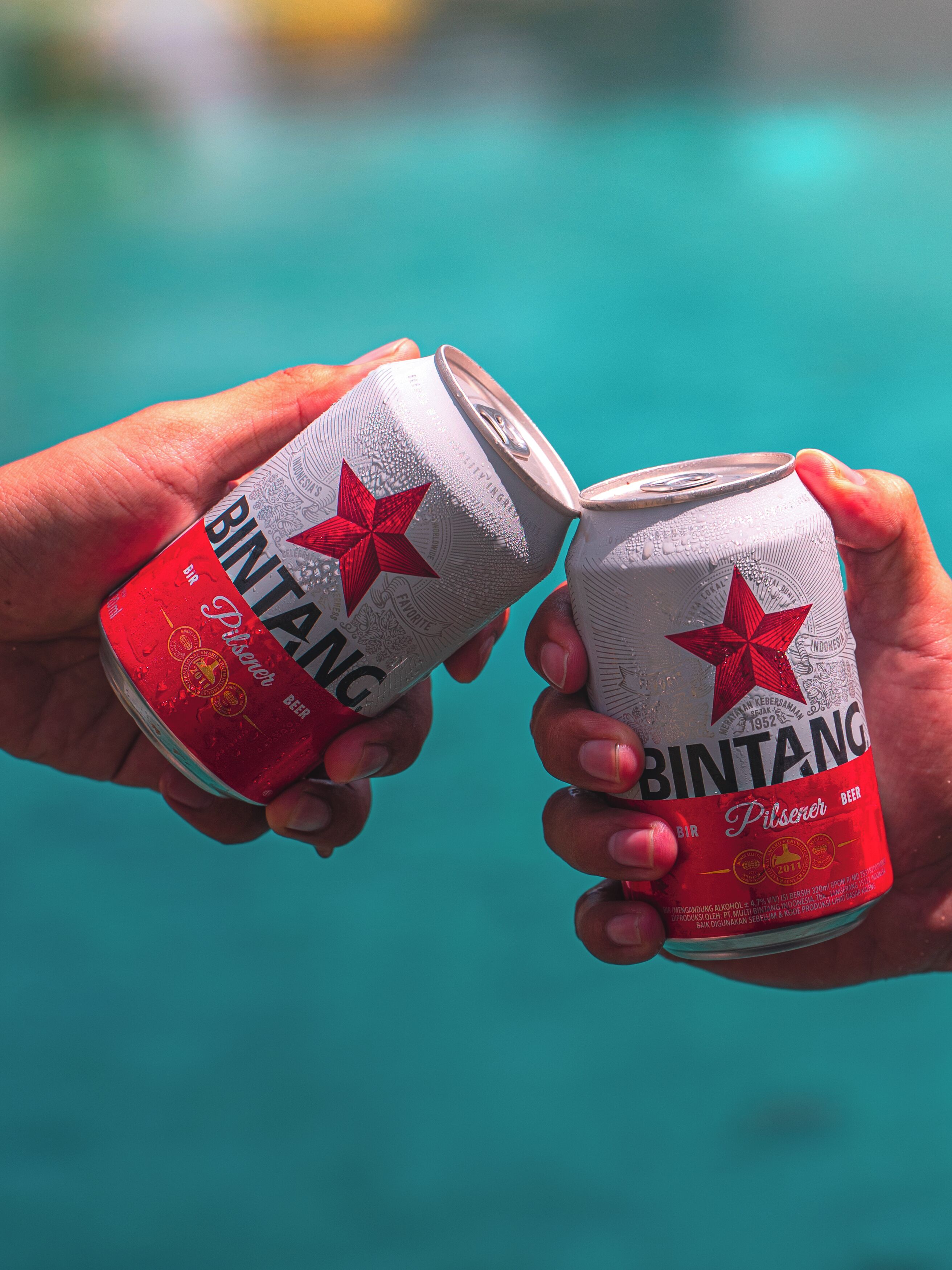 Two hands holding a can of Bintang beer.