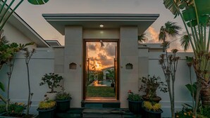 A modern entrance with a glass door, surrounded by potted plants and a pathway leading to a garden. - Theodosia Villa (Kutuh)