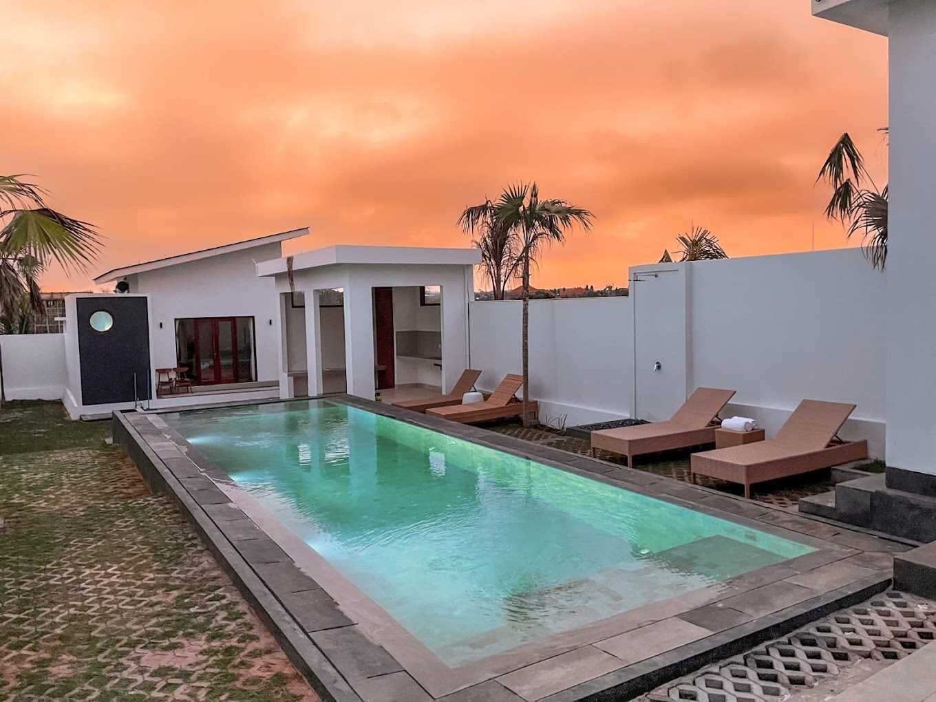 A modern outdoor swimming pool with lounge chairs and a white building in the background.
