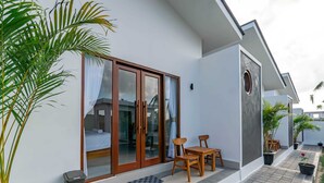 A modern hotel room with a large sliding glass door, a small balcony with a table and chairs, and a potted plant. - Theodosia Villa (Kutuh)