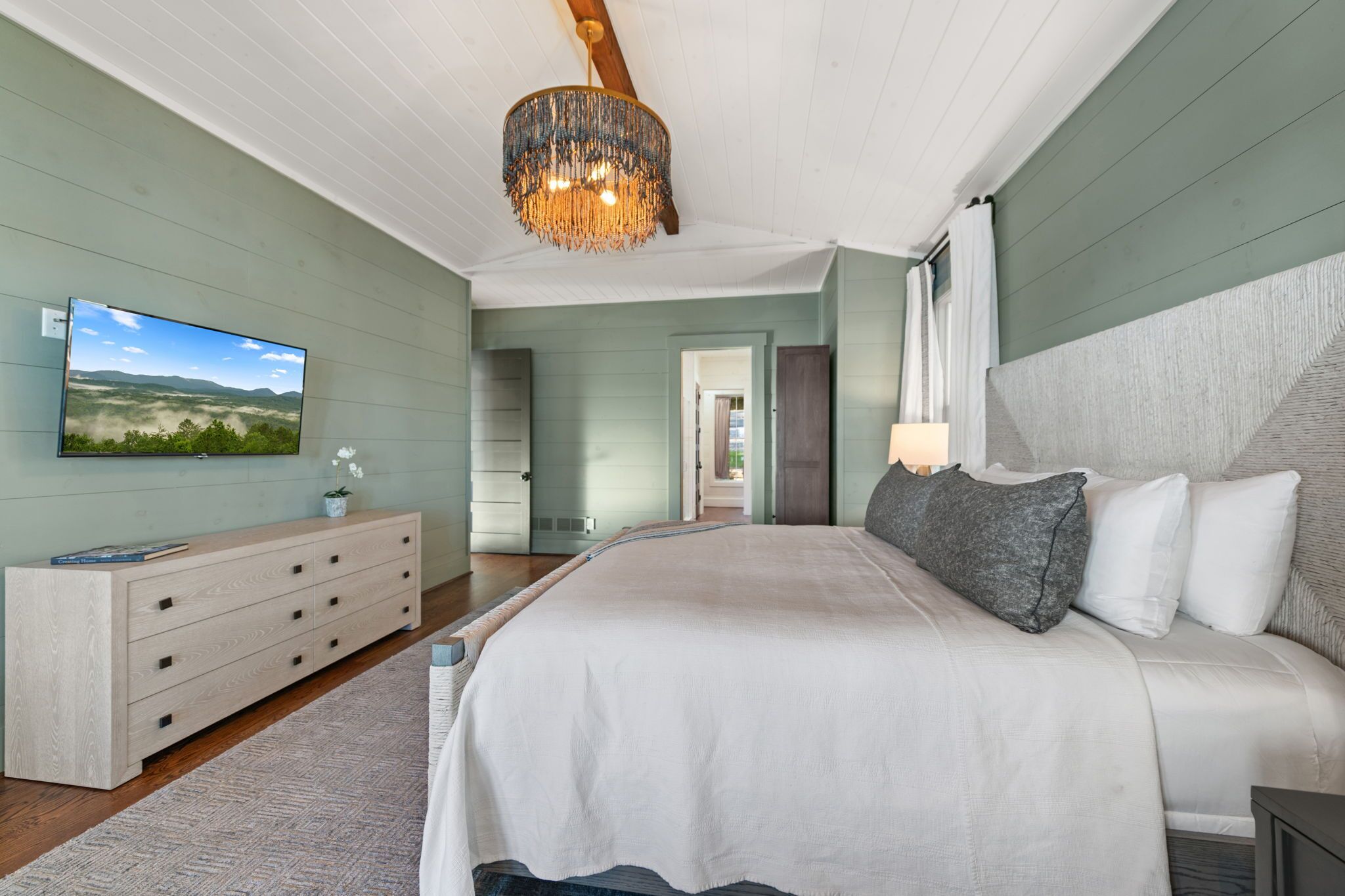 A bedroom with a large bed, a dresser, a television, and a chandelier.