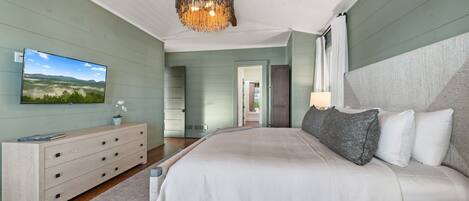 A bedroom with a large bed, a dresser, a television, and a chandelier.