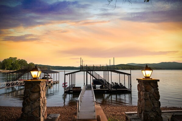 A wooden dock leading to a stone pier with a gazebo, surrounded by calm water and a sunset sky.