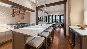 A modern kitchen with a large island, wooden beams, and hanging copper pots. - Lakeview Landing -Lakefront, Private Dock, Wood Burning Fireplace (Morganton)
