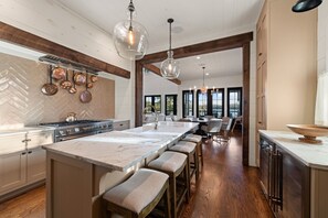 A modern kitchen with a large island, wooden beams, and hanging copper pots.