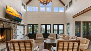 A spacious living room with a stone fireplace, comfortable seating, and a large TV on the wall. - Lakeview Landing -Lakefront, Private Dock, Wood Burning Fireplace (Morganton)