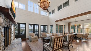 A spacious living room with a stone fireplace, large windows, and a high ceiling. - Lakeview Landing -Lakefront, Private Dock, Wood Burning Fireplace (Morganton)