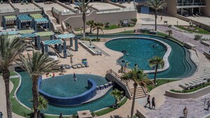 A resort with a large pool area, outdoor seating, and palm trees.