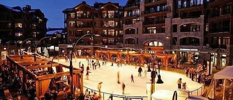 Ein Hotel mit mehreren Balkonen, einem Innenhof mit Eislaufbahn und Außenbereichen mit Sitzgelegenheiten.