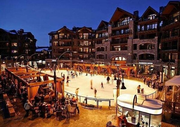 A hotel with multiple balconies, a central courtyard with a skating rink, and outdoor seating areas.