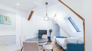 A modern loft bedroom with a skylight, a round dining table, and a blue sofa.