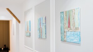 A hallway with white walls and a wooden ceiling. There are three artworks displayed on the wall.