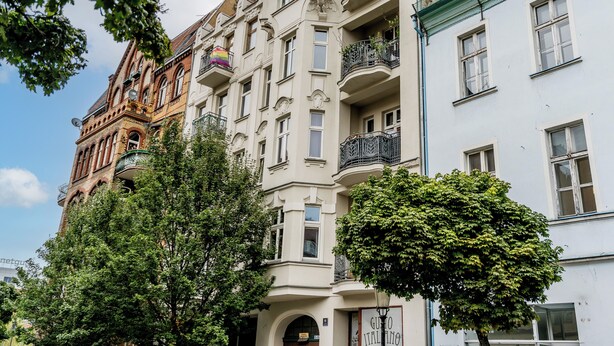 A multi-story building with balconies, a sign reading "GUMO ITALIANO," and trees in front.