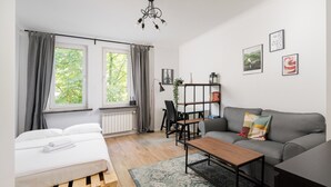 A modern living room with a bed, a sofa, a coffee table, and a bookshelf. - Grójecka City Gateway Apartment (Warszawa)