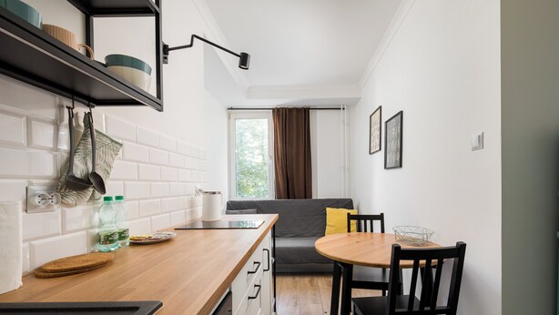 A compact kitchen with a wooden countertop, a built-in shelf, and a window with curtains. - Grójecka City Gateway Apartment (Warszawa)