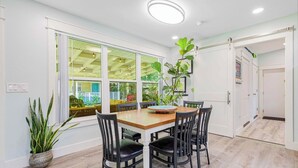 Comedor con mesa de madera, sillas negras, ventanas amplias con vistas a zonas verdes y una lámpara de techo.