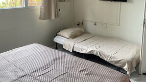 Une chambre à coucher avec un lit, un ventilateur de plafond, un téléviseur fixé au mur et une fenêtre avec des rideaux.