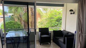 Un salon moderne doté d’une porte-fenêtre coulissante donnant sur un balcon. La pièce est aménagée avec une table à plateau en verre, un canapé noir et un petit fauteuil noir.