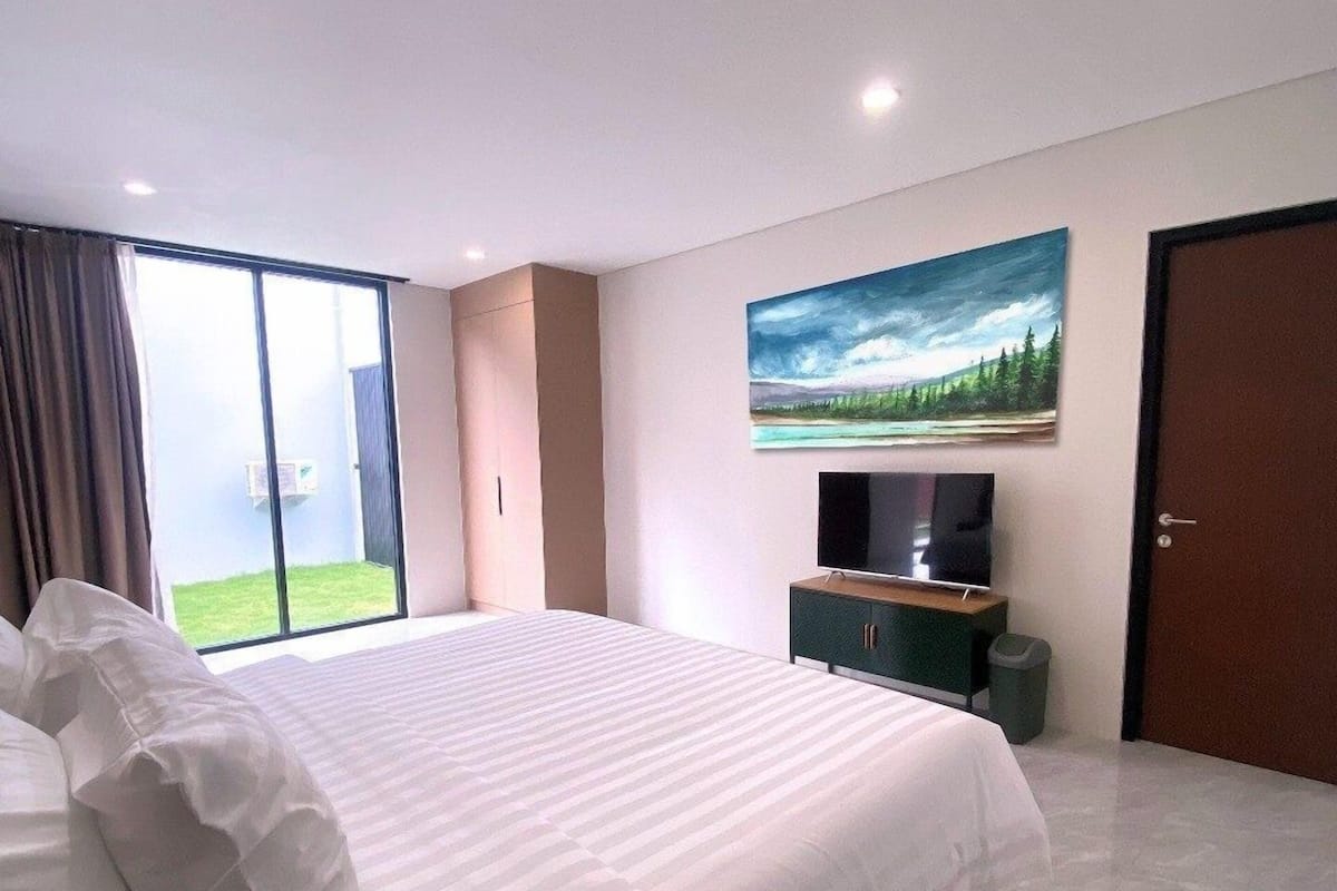 Une chambre moderne avec un grand lit, un téléviseur à écran plat, un tableau et une porte-fenêtre coulissante donnant sur un balcon.