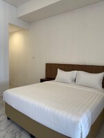 A neatly made bed with a wooden headboard, a bedside table, and a marble floor.