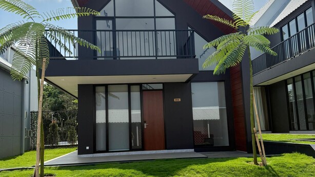 A modern two-story house with a balcony, a stone wall in front, and a well-maintained lawn. - Wind Hill Mountain View Resort (Megamendung)