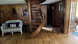 A wooden interior with a spiral staircase, a white wicker sofa, and a red chair. - Charming Cabin, Lake Access! Backyard Bubbling Brook. Pets Welcome! (Denmark)