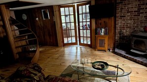 A cozy living room with a wooden staircase, a glass coffee table, a fireplace, and a bookshelf. - Charming Cabin, Lake Access! Backyard Bubbling Brook. Pets Welcome! (Denmark)