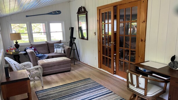 A cozy living room with a sofa, a rocking chair, a telescope, and a large wooden door. - Charming Cabin, Lake Access! Backyard Bubbling Brook. Pets Welcome! (Denmark)