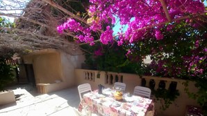 Eine Terrassensitzgruppe im Freien mit Esstisch, umgeben von einer Wand mit Verzierungen und einem Baum mit violetten Blüten.