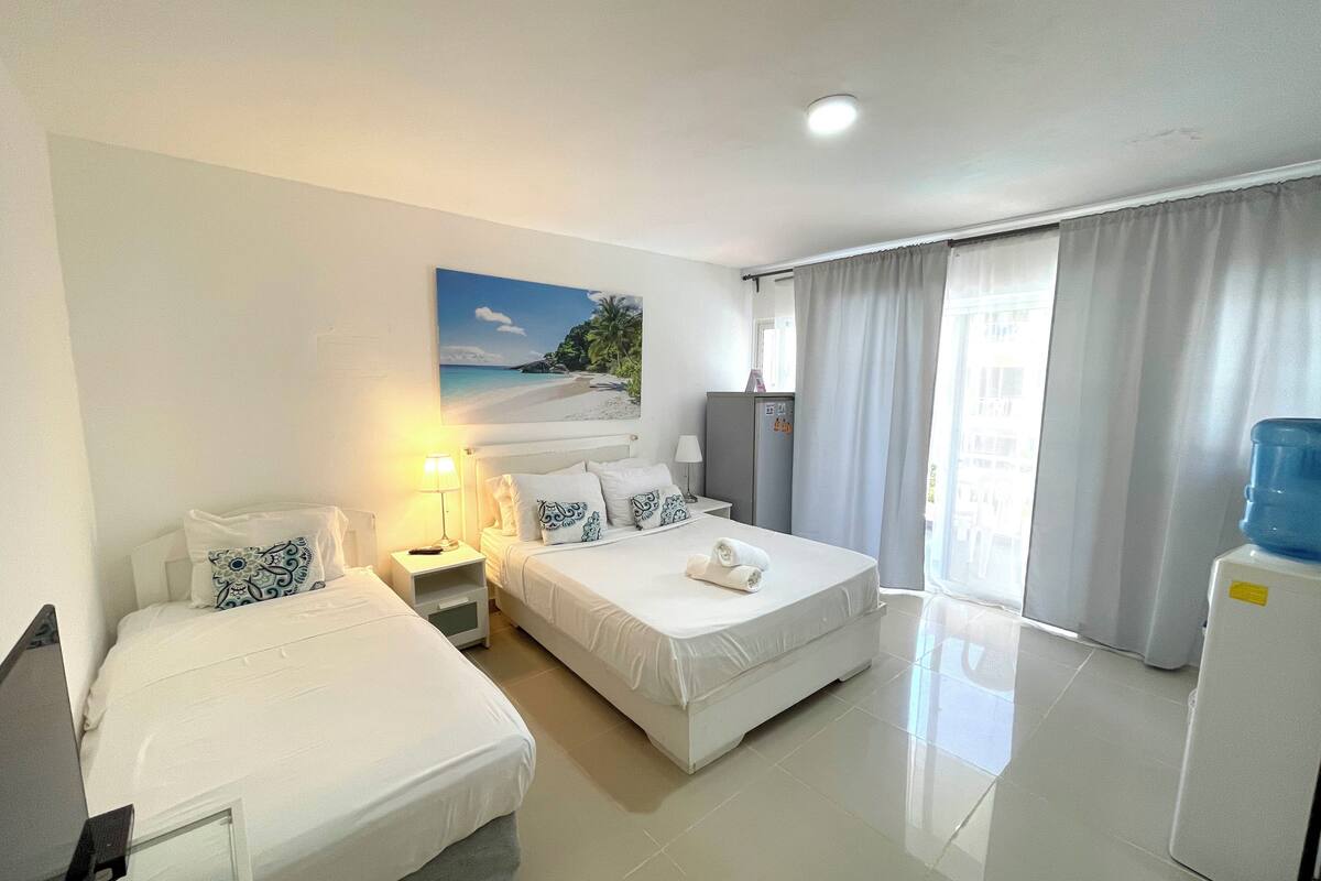 Een hotelkamer met twee bedden, een bureau, een waterdispenser en een schilderij van een strandgezicht.