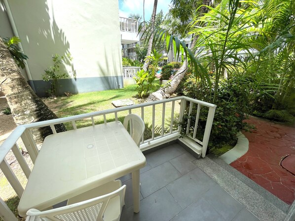Un pequeño patio al aire libre con una mesa y sillas, rodeado de exuberante vegetación y una vista de un edificio al fondo.