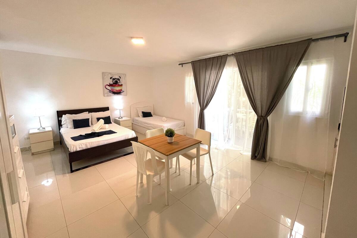 Een hotelkamer met een bed, nachtkastje, lamp en een zithoek met een tafel en stoelen.