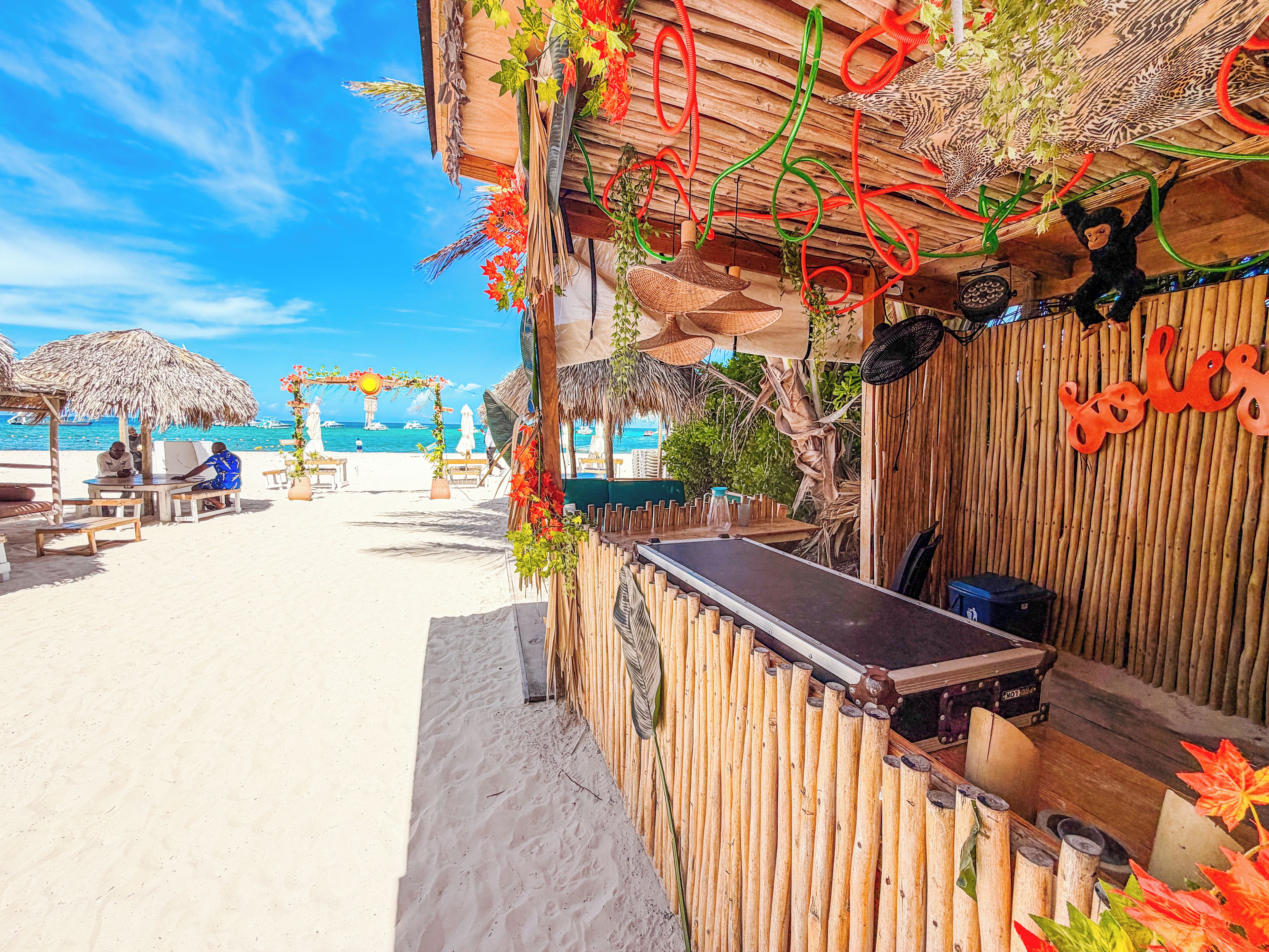 Eine Strandbar mit Holzbauweise, einem Reetdach und einem Schild mit der Aufschrift 'Tales'.